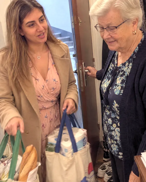 Une voisine apporte deux sacs de courses à une dame âgée, sur le pas de sa porte