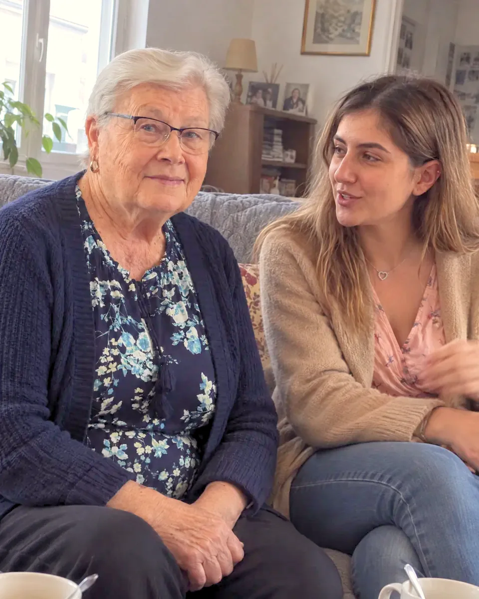 Une dame âgée et une jeune femme discutent, assises sur un canapé